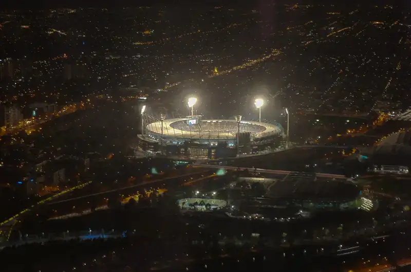 A cricket stadium under floodlights, seen from above at night