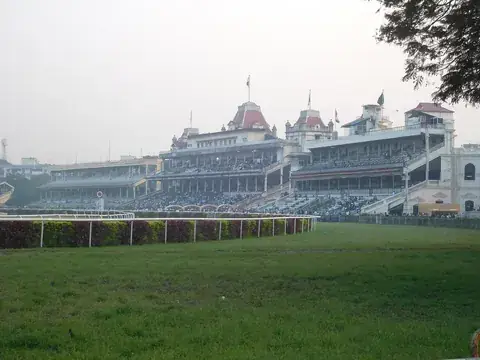 The Victorian grandstands of the Kolkata racecourse, with red-roofed towers, seen across green turf on a hazy day