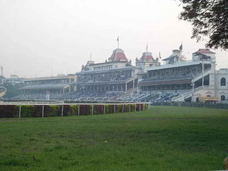 The Victorian grandstands of the Kolkata racecourse, with red-roofed towers, seen across green turf on a hazy day