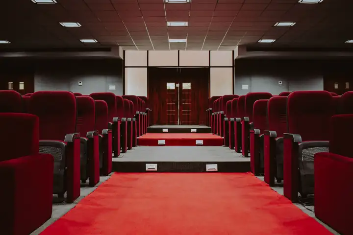 Rows of empty red velvet seats either side of a red-carpet aisle