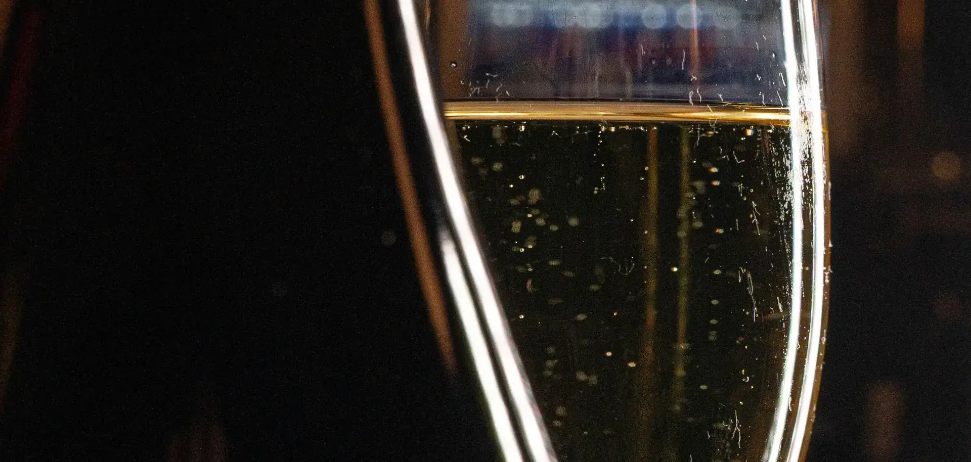 A glass of sparkling wine beside a dark bottle at a bar