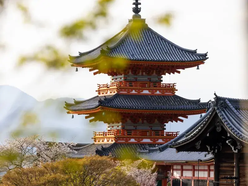 A red pagoda at Kiyomizu-dera in Kyoto, framed by spring blossom and green leaves