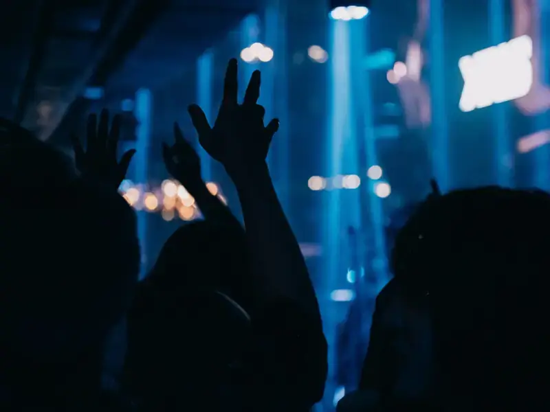 Concert-goers seen from behind, hands raised under blue stage light