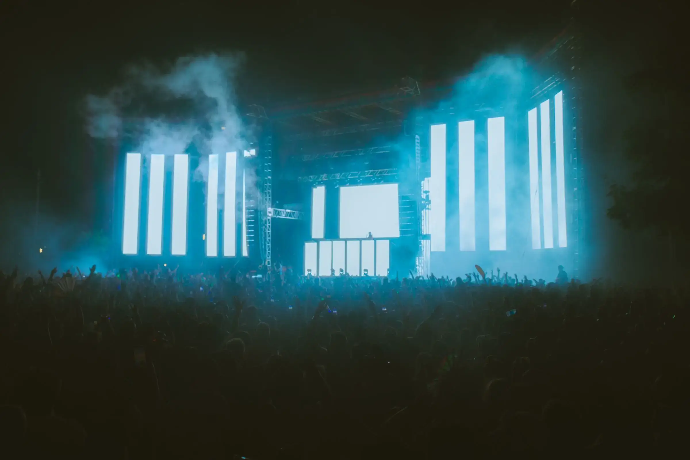 A festival stage glowing through haze above a night crowd